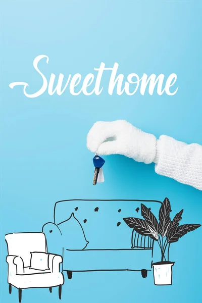 Cropped view of woman in white glove holding key near sweet home lettering and sofa illustration on blue — Stock Photo