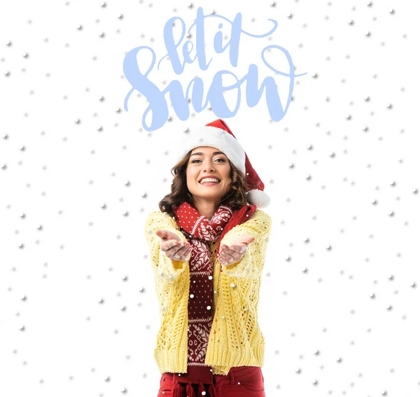 Joyeuse jeune femme en santa chapeau et écharpe debout avec les mains tendues près qu'il neige lettrage sur blanc — Photo de stock
