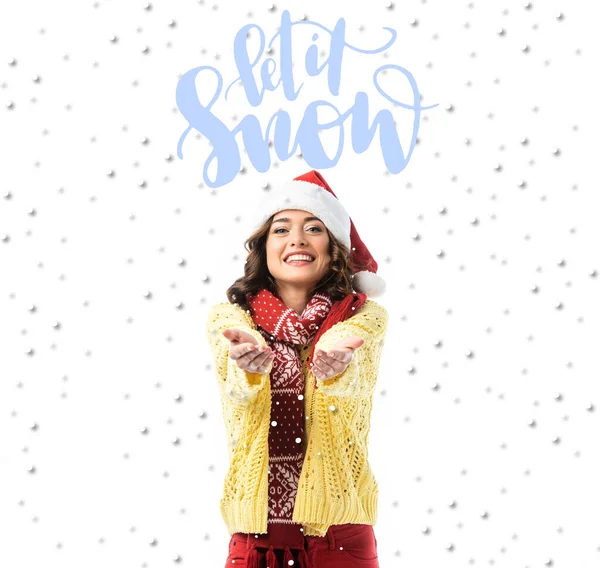 Joyful young woman in santa hat and scarf standing with outstretched hands near let it snow lettering on white — Stock Photo