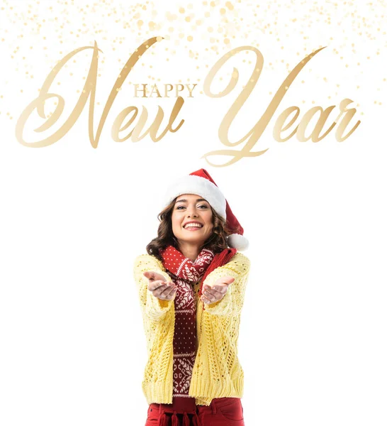 Freudige junge Frau mit Weihnachtsmütze und Schal, die mit ausgestreckten Händen in der Nähe eines frohen Neujahrsschreibens auf weißem Grund steht — Stockfoto