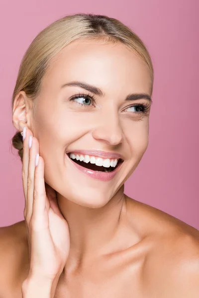 Sonriente hermosa mujer rubia tocando la cara aislado en rosa - foto de stock