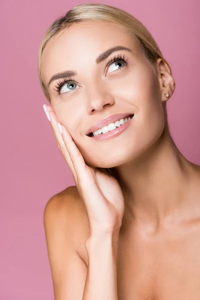 Smiling beautiful blonde woman touching face isolated on pink — Stock Photo