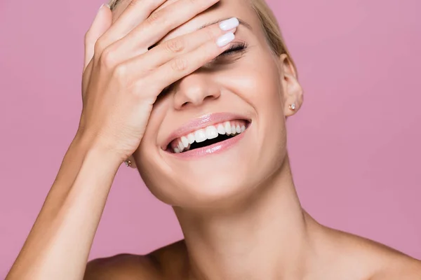 Sorrindo bela mulher loira posando com a mão no rosto isolado em rosa — Fotografia de Stock