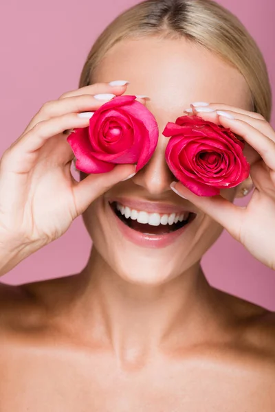 Smiling beautiful blonde woman with rose flowers on eyes isolated on pink — Stock Photo