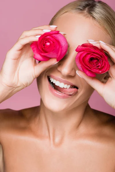 Lächelnd schöne blonde Frau mit Rosenblüten auf Augen isoliert auf rosa — Stockfoto