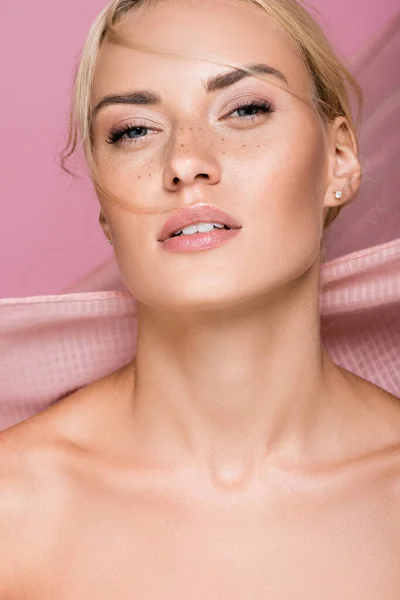 Beautiful blonde woman with freckles and bare shoulders near curtain isolated on pink — Stock Photo