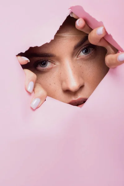 Hermosa mujer con pecas en agujero de papel rosa - foto de stock