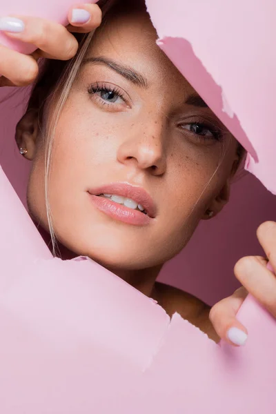 Belle femme avec des taches de rousseur dans le trou de papier rose — Photo de stock