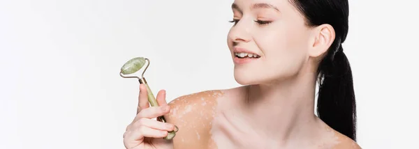 Sorrindo jovem mulher bonita com vitiligo segurando rolo de jade no rosto isolado no branco, banner — Fotografia de Stock