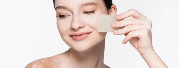 Smiling young beautiful woman with vitiligo using gua sha isolated on white, banner — Stock Photo