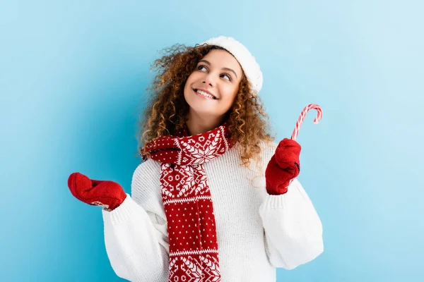 Cheerful woman in red mittens holding candy cane on blue — Stock Photo