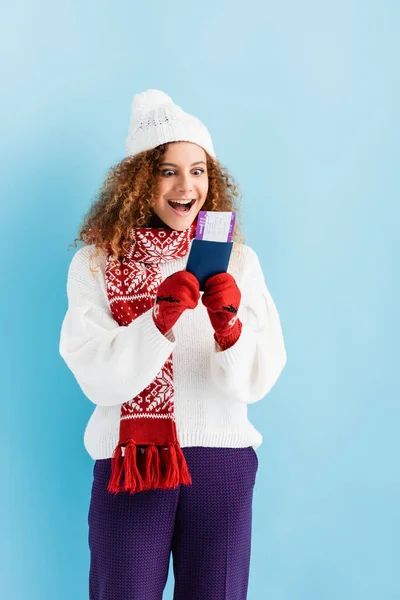 Mujer joven excitada en sombrero y suéter con pasaporte en azul - foto de stock