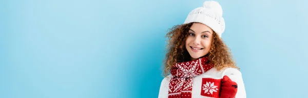 Cheerful young woman in hat and sweater holding cup in knitted holder on blue, banner — Stock Photo