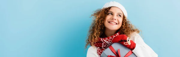 Smiling woman in hat holding wrapped gift box on blue, banner — Stock Photo
