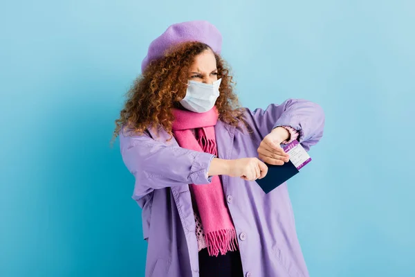 Mujer enojada en boina, bufanda, máscara médica y pasaporte de rasgadura de abrigo en azul - foto de stock