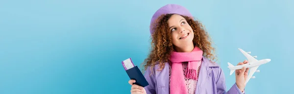 Улыбающаяся женщина в берете, шарфе и пальто с паспортом и игрушечным самолетом на синем, баннер — стоковое фото