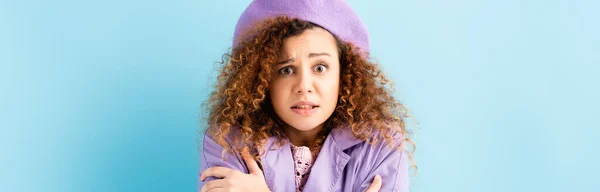 Curly woman in beret freezing and embracing herself on blue background, banner — Stock Photo