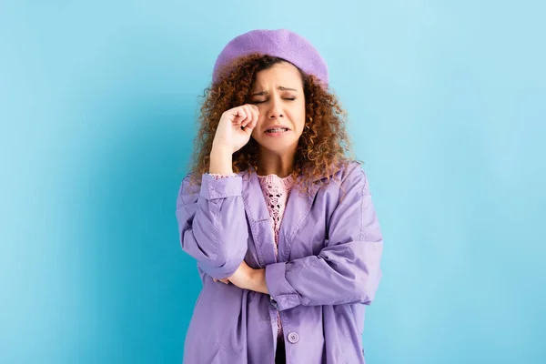 Upset young woman in beret crying on blue background — Stock Photo