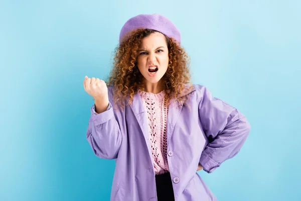 Angry woman in beret showing clenched fist on blue — Stock Photo