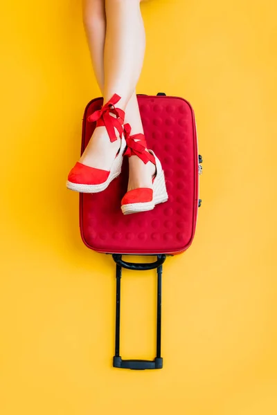 Вид зверху на жінку в клинових сандалі біля червоної валізи на жовтому — Stock Photo