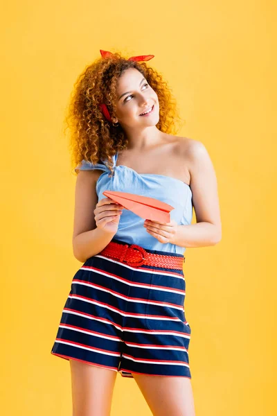 Fröhliche junge Frau im Sommer-Outfit mit Papierflieger auf gelb — Stockfoto