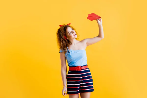 Happy young woman in summer outfit holding paper plane on yellow — Stock Photo