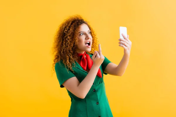 Maleducata giovane donna mostrando dito medio mentre prende selfie su giallo — Foto stock