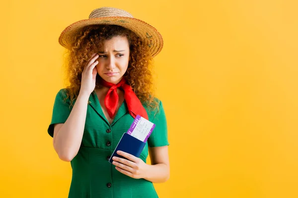 Frustrated woman in straw hat and dress holding passport isolated on yellow — Stock Photo