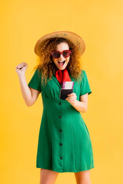 Amazed woman in straw hat, sunglasses and dress holding passport on yellow — Stock Photo