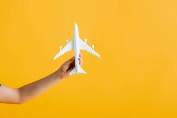 Vista parcial de mujer sosteniendo avión de juguete aislado en amarillo - foto de stock