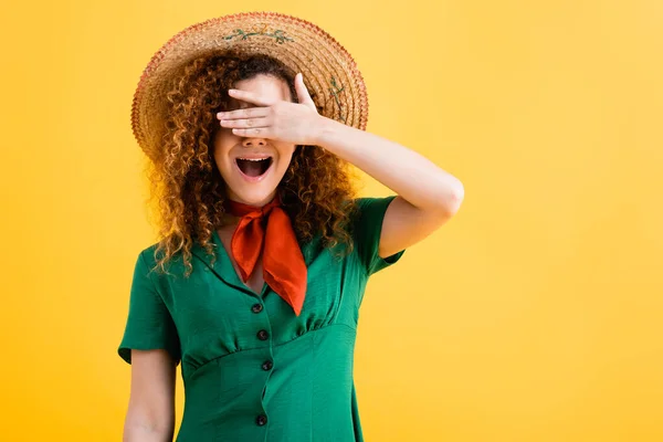 Mujer joven excitada en sombrero de paja que cubre los ojos aislados en amarillo - foto de stock