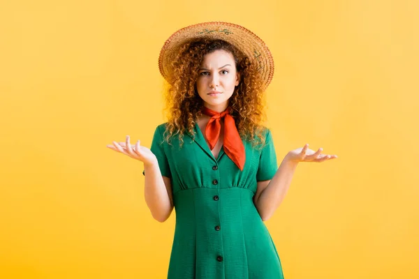 Confused young woman in straw hat and green dress gesturing on yellow — Stock Photo