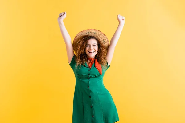 Amazed woman in green dress and straw hat standing with hands above head on yellow — Stock Photo