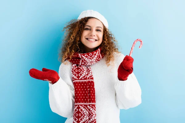 Young cheerful woman in red mittens holding candy cane on blue — Stock Photo