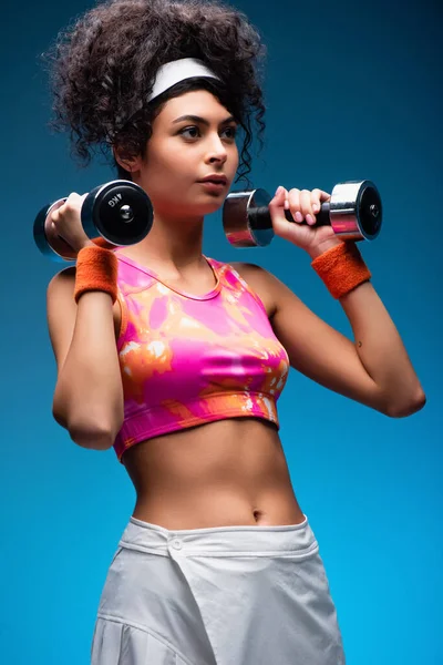 Curly young woman exercising with dumbbells on blue — Stock Photo