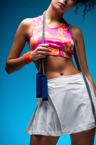 Cropped view of curly young woman standing with skipping rope on blue — Stock Photo
