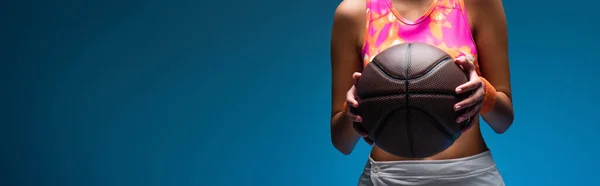 Cropped view of young woman in sportswear holding basketball on blue, banner — Stock Photo