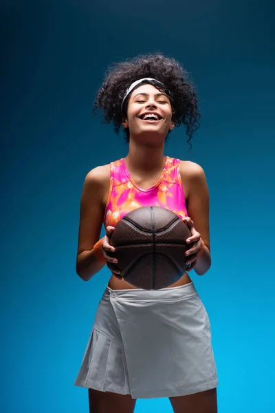 Sonriente mujer en ropa deportiva celebración de baloncesto en azul - foto de stock