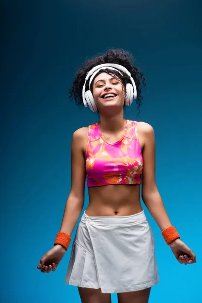 Donna sorridente in abbigliamento sportivo ascoltare musica in cuffie senza fili su blu — Foto stock