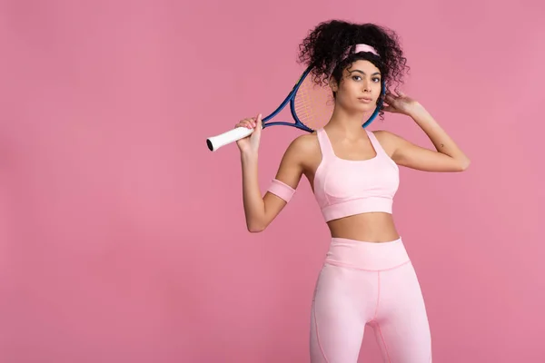 Encaracolado jovem desportista segurando raquete de tênis enquanto de pé isolado em rosa — Fotografia de Stock