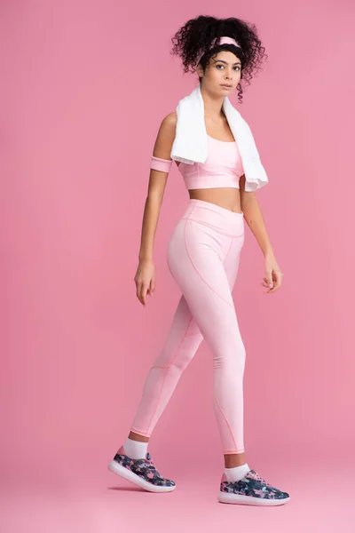 Curly young sportswoman with towel on shoulders walking on pink — Stock Photo