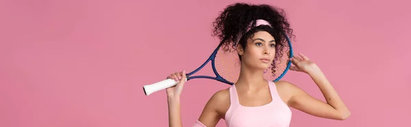 Curly young sportswoman holding tennis racket isolated on pink, banner — Stock Photo