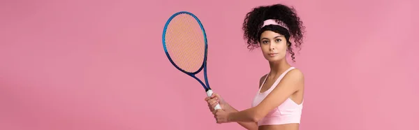 Young curly sportswoman holding tennis racket while playing isolated on pink, banner — Stock Photo