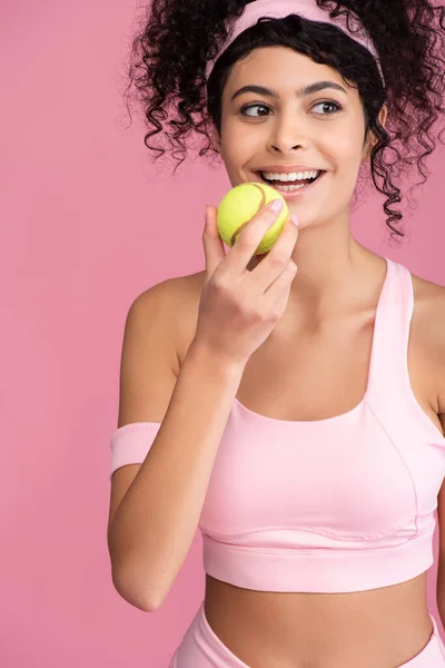 Радостная молодая женщина держит теннисный мяч изолирован на розовый — стоковое фото