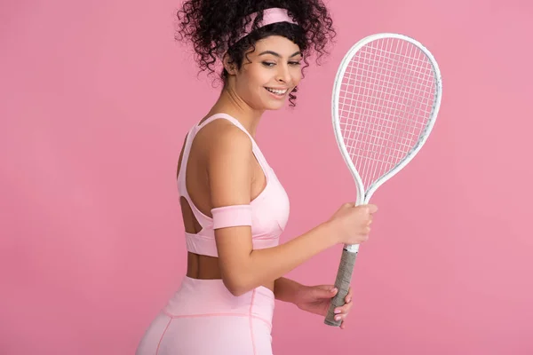 Sonriente joven deportista sosteniendo raqueta de tenis aislada en rosa - foto de stock