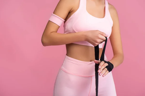 Vista parcial de la mujer deportiva en la mano de envoltura de ropa deportiva con bondage aislado en rosa - foto de stock