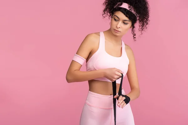 Lockige Frau in Sportbekleidung, die Hand mit Fesseln umwickelt, isoliert auf rosa — Stockfoto