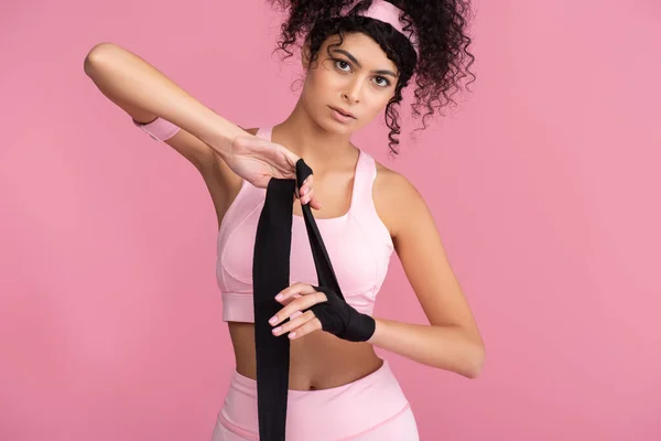 Lockige junge Frau in Sportbekleidung, die Hand mit schwarzer Fessel auf rosa isoliert — Stockfoto