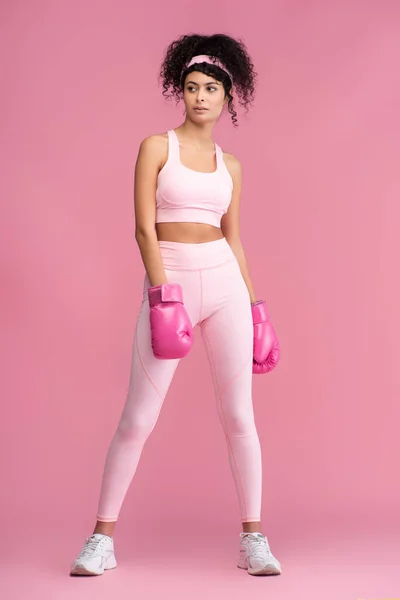 Pleine longueur de jeune femme bouclée en vêtements de sport et gants de boxe sur rose — Photo de stock