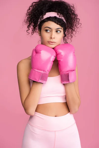 Ricci giovane donna in abbigliamento sportivo e guanti da boxe guardando lontano isolato sul rosa — Foto stock